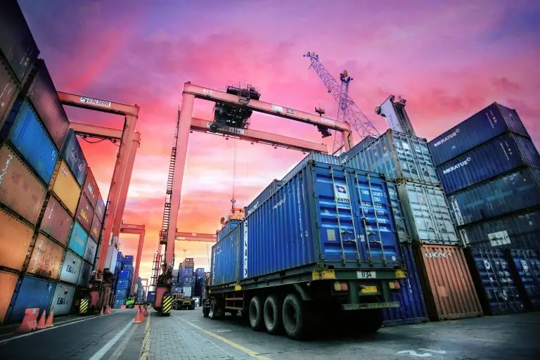 Shipping containers stacked at busy port terminal at sunset